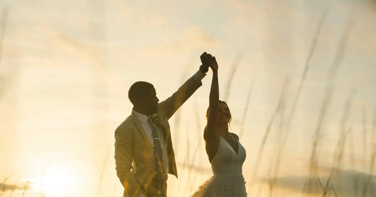 Bruidspaar danst in een veld bij zonsondergang, het moment dat gasten fotograferen